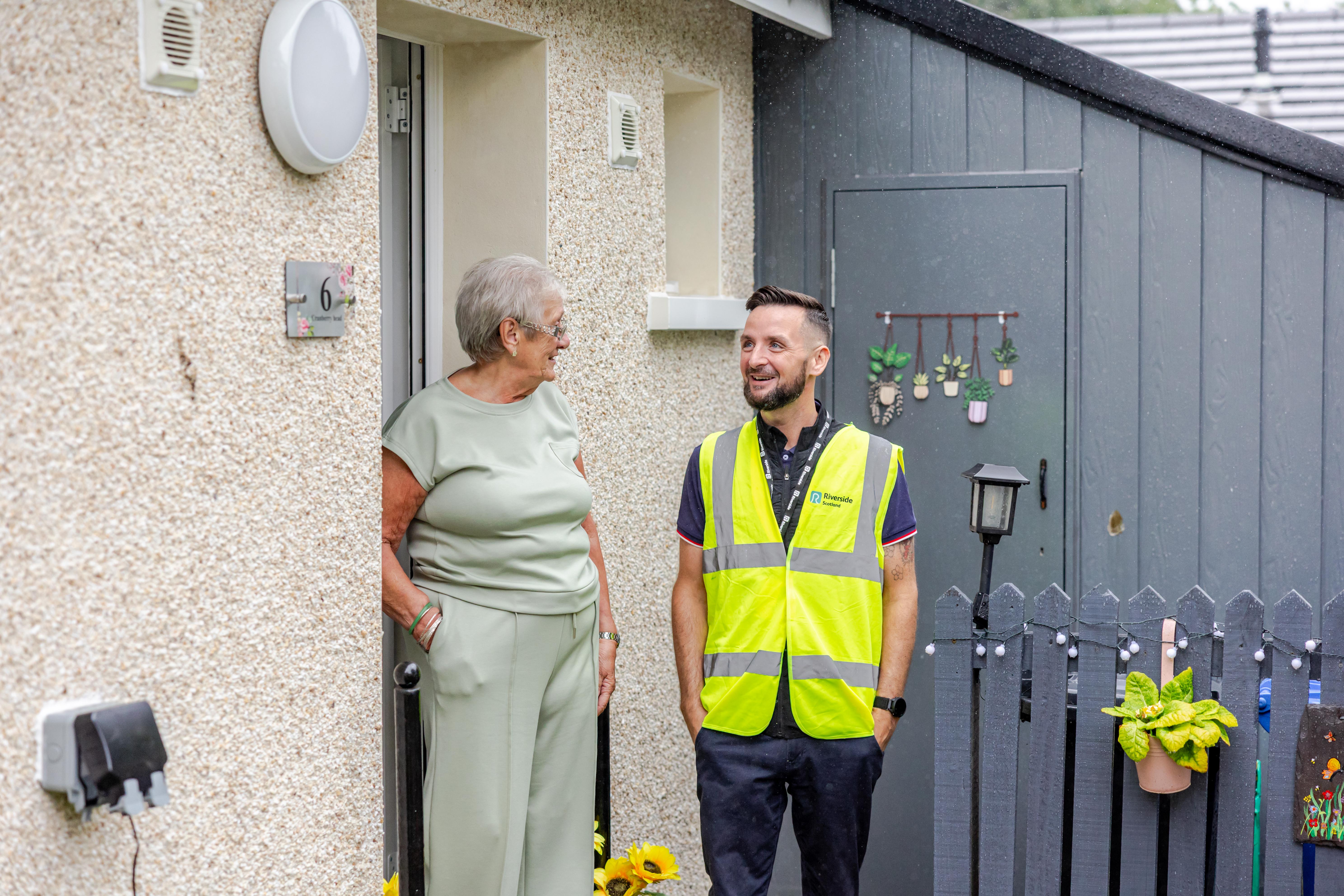 Two people stand chatting in a doorway one wears a hi-vis vest