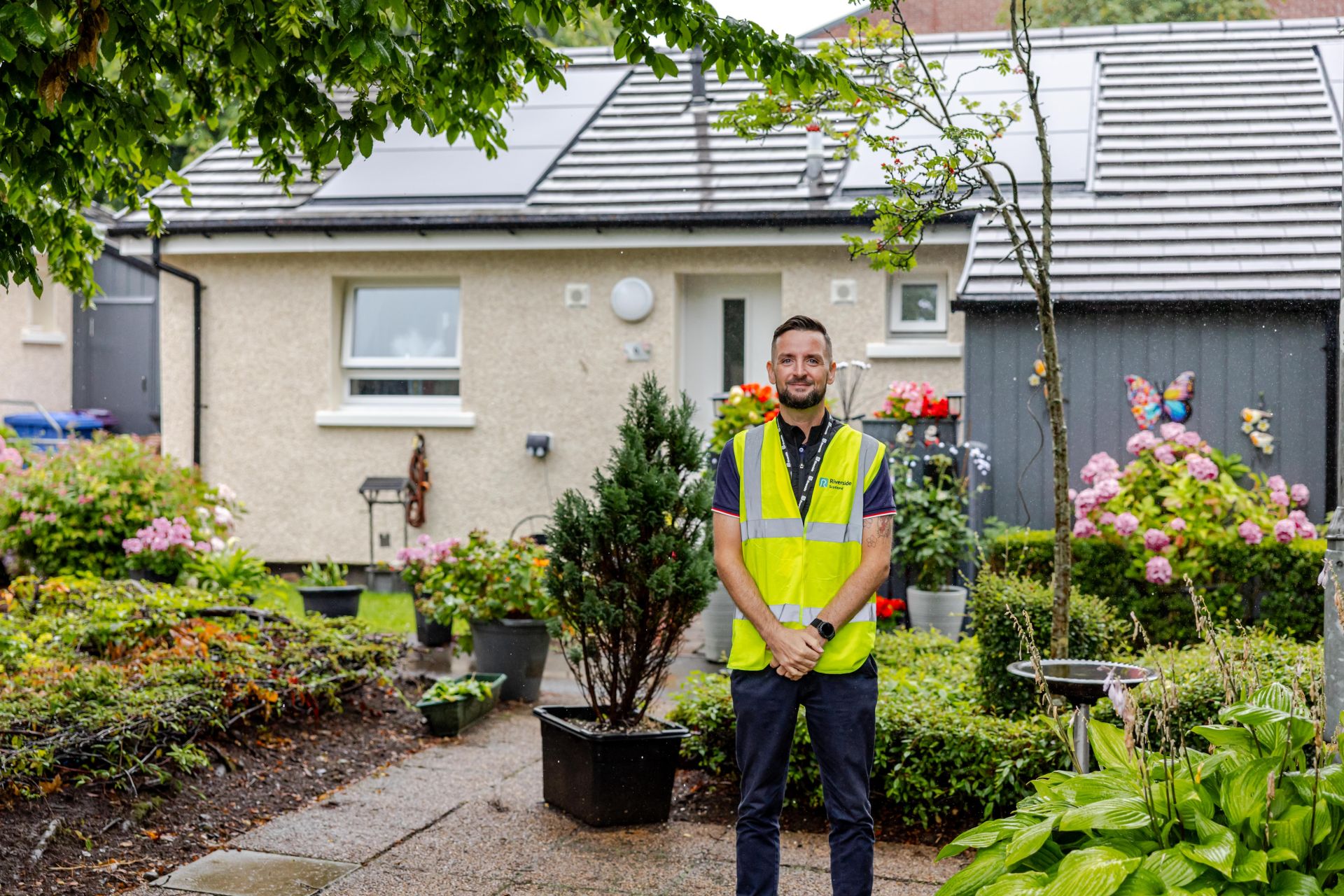 A person in a hi-vis stands infront of a house with solar panels