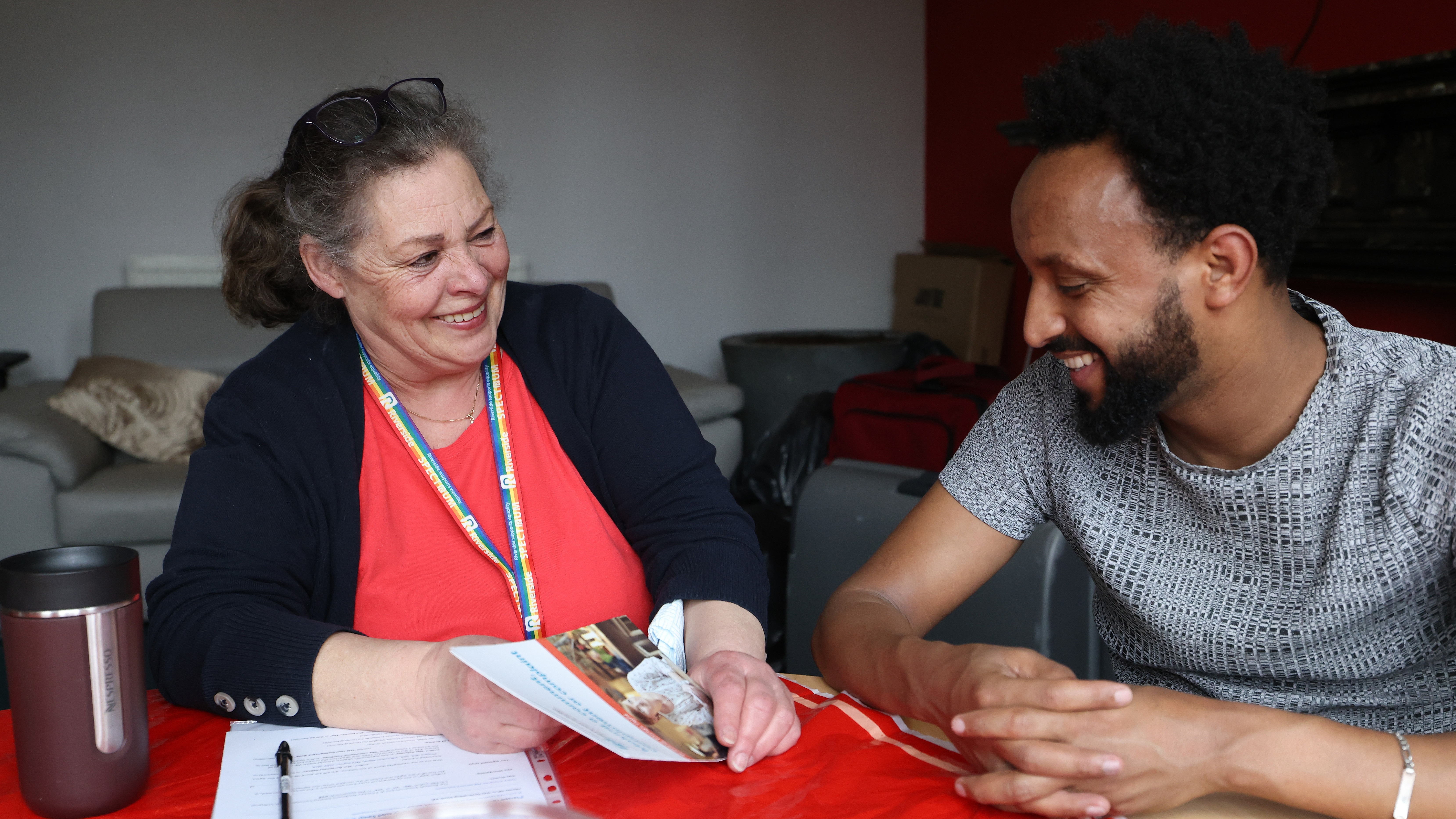 A Riverside staff member speaking to a resident, sat at a dining table.