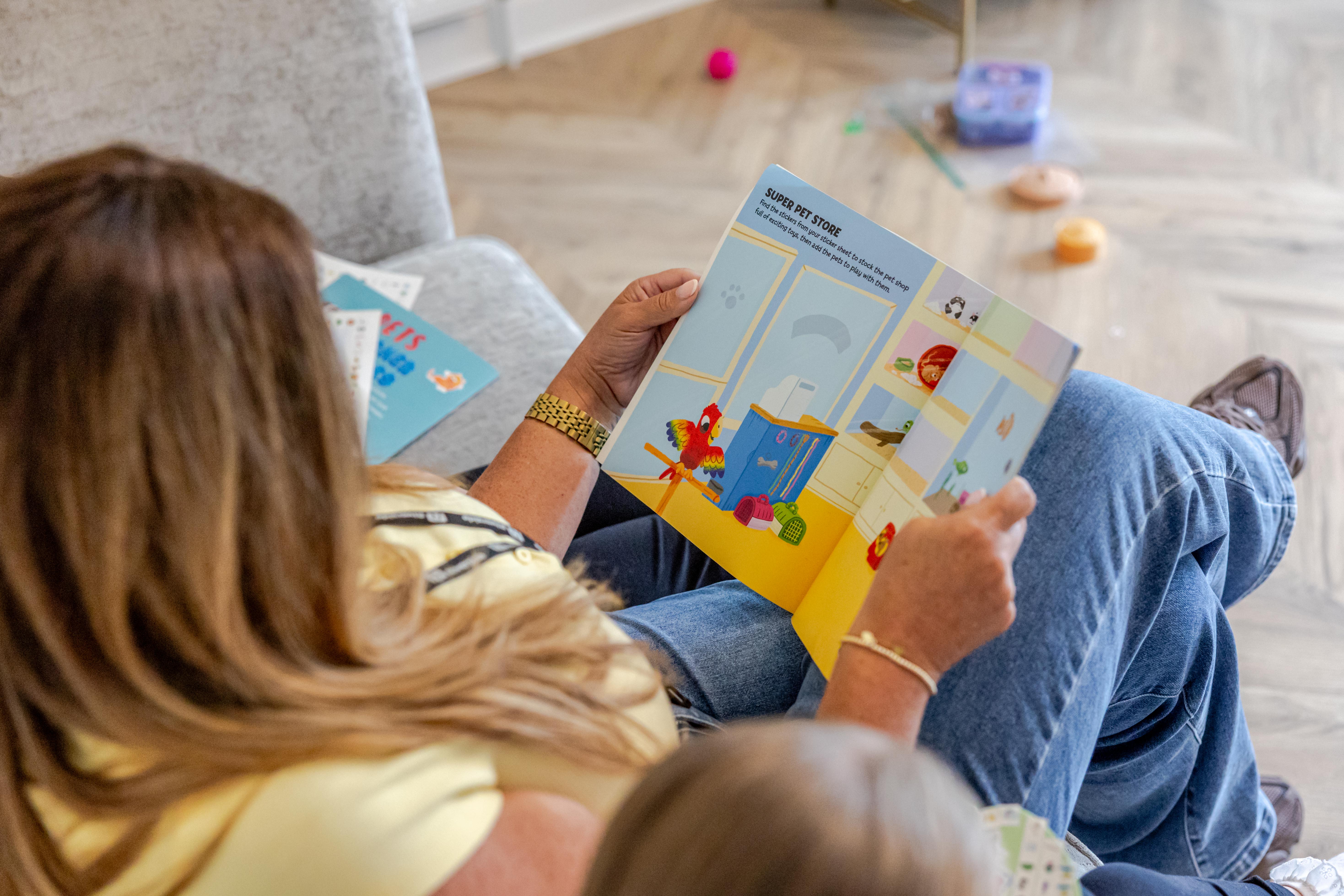 A person sits on a sofa reading a children's book