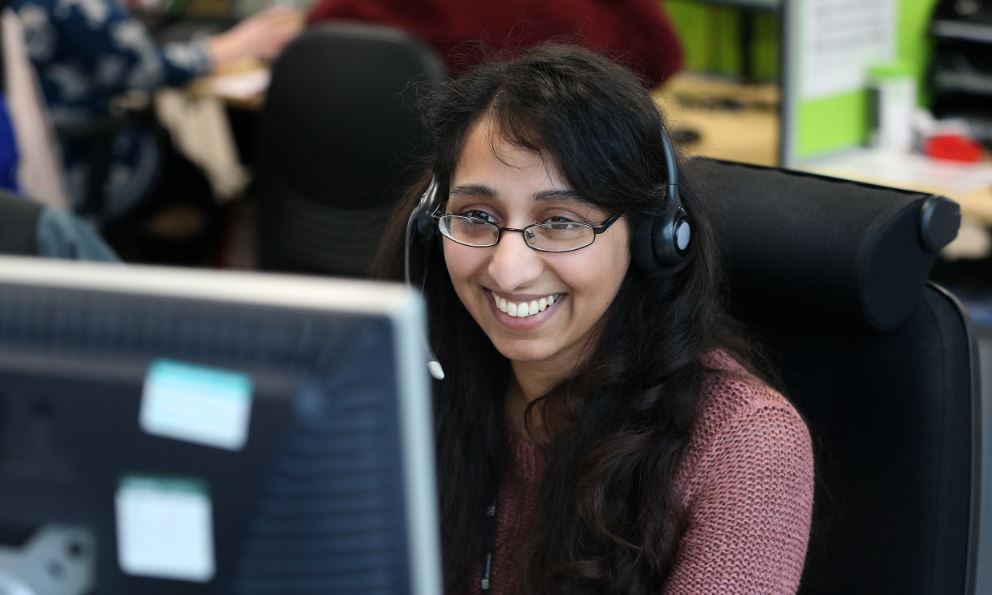 A customer service agent with a phone headset, sat at their desk.